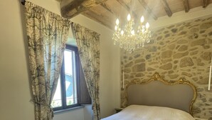 Une chambre avec un mur en pierre, des poutres en bois, un lustre et un grand lit.