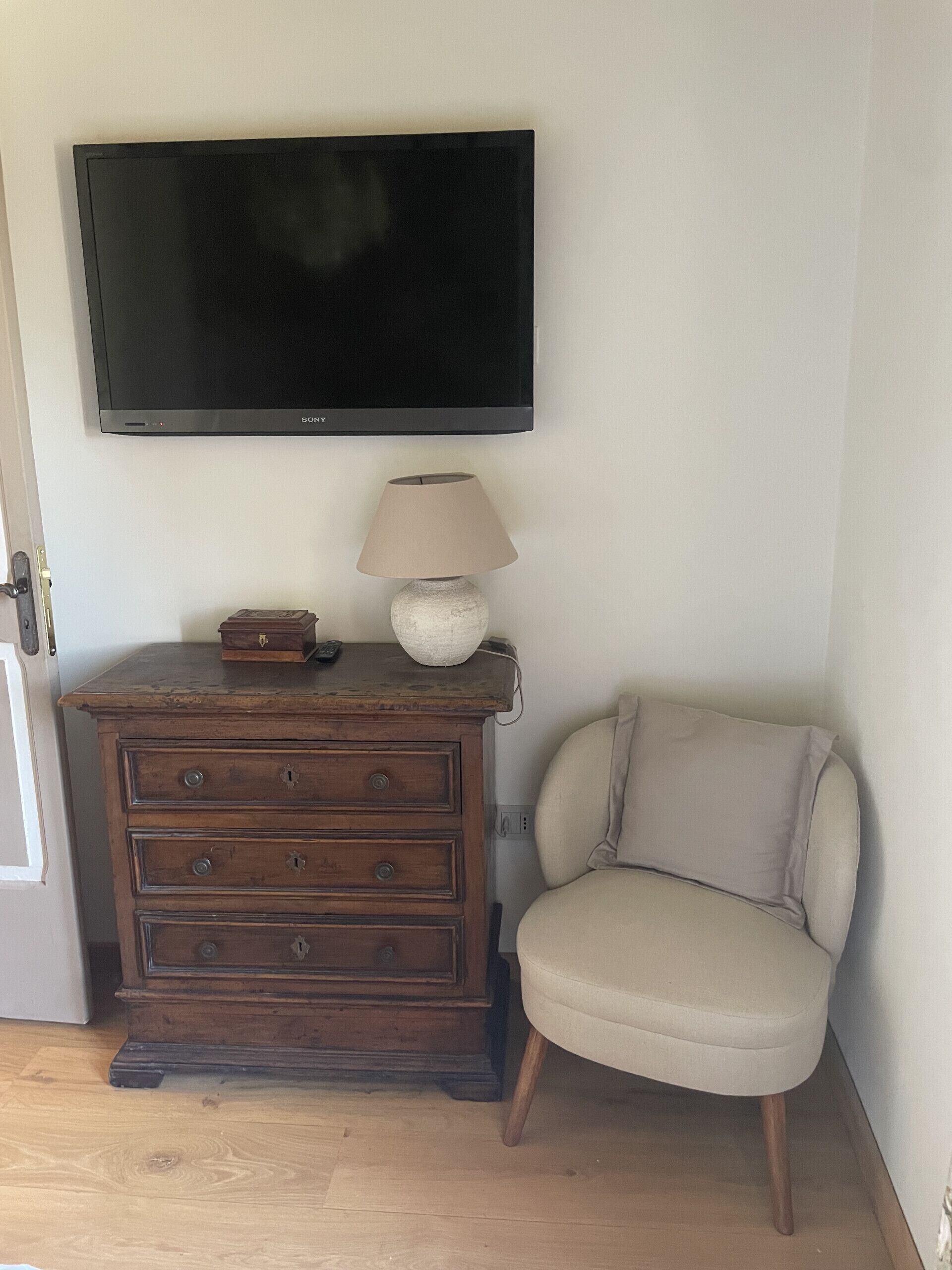 Een kamer met een houten dressoir, een beige fauteuil en een flatscreen televisie aan de muur.