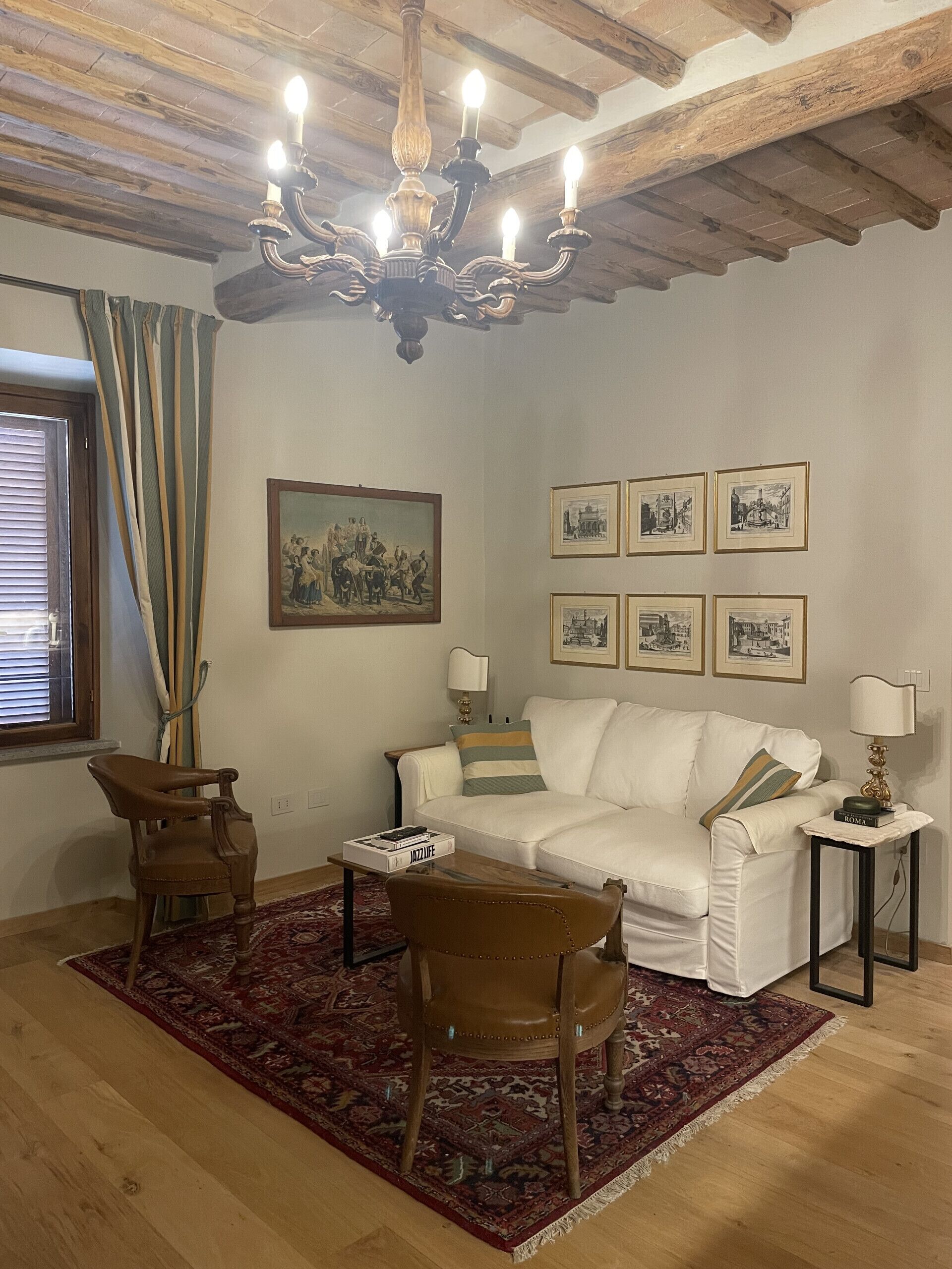 A living room with a white sofa, a wooden coffee table, a brown leather chair, a chandelier, and a patterned rug.