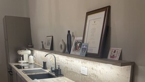 Une cuisine avec un long plan de travail, un évier et une machine à café. Des certificats encadrés sont accrochés au mur.