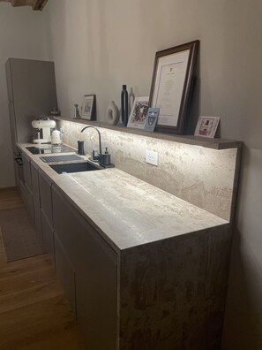 Eine Küche mit einer langen Arbeitsplatte, einem Spülbecken und einer Kaffeemaschine. An der Wand hängen gerahmte Zertifikate.