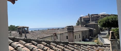 A view from a covered terrace overlooking a historic town with terracotta roof tiles and traditional buildings.