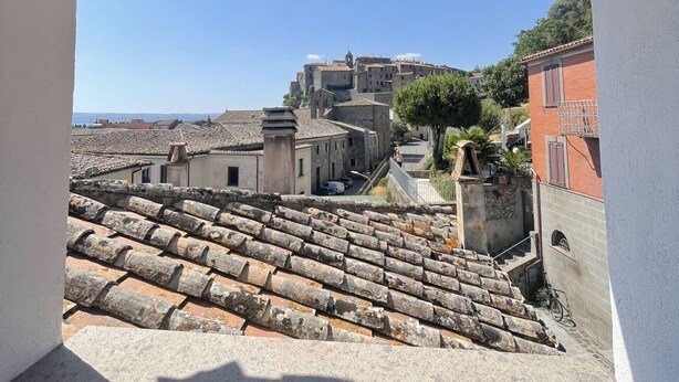 Une vue depuis un balcon doté d’un plafond en bois, donnant sur une ville historique avec des toits en tuiles de terre cuite et des bâtiments traditionnels.