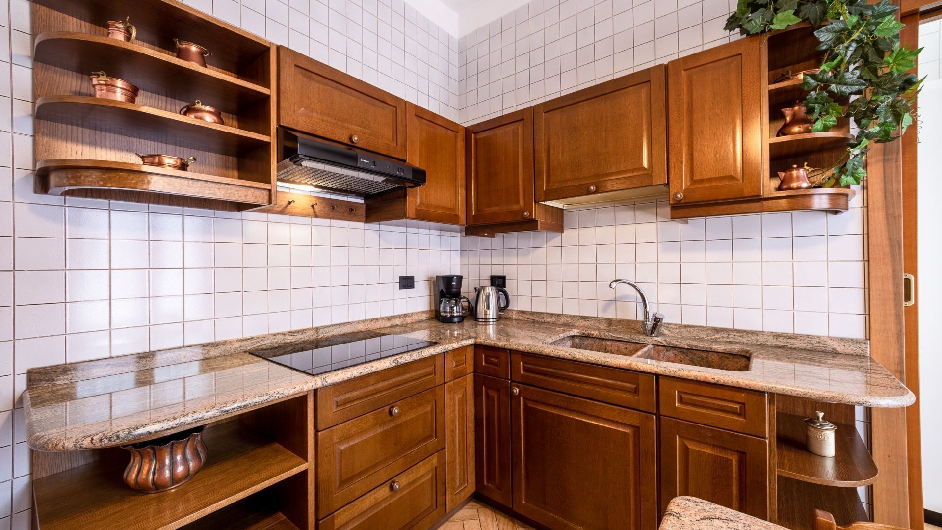 Cuina amb armaris de fusta, respold d'azulejos blancs, encimera de granat i cafetera.