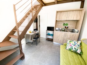 A compact living space with a staircase, a dining area, a kitchenette, and a green sofa with a cactus-pattern pillow. - New Agriloft 5 Mare Clima e giardino, sea at 50m (Bordighera)