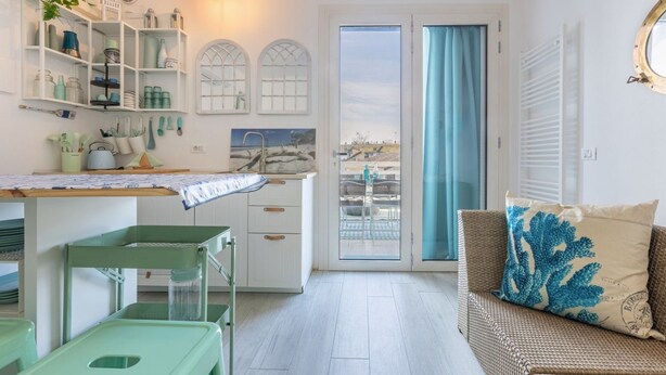 Ein Zimmer mit Küchenzeile, einem Esstisch, einer Couch mit Kissen und Blick durch eine Glastür.