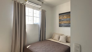 Un dormitorio con cama, cortinas, una ventana y un cuadro en la pared.