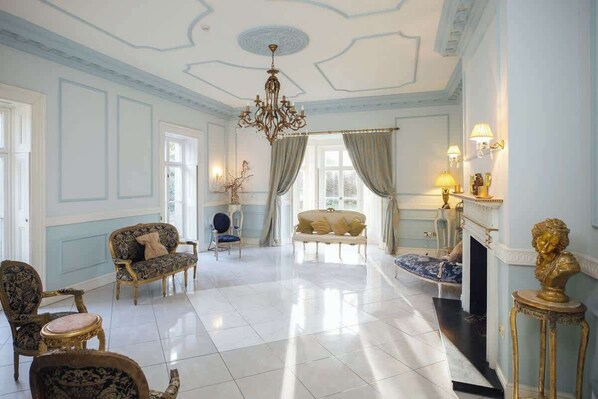 A spacious room with a chandelier, a fireplace, and a large window with curtains.