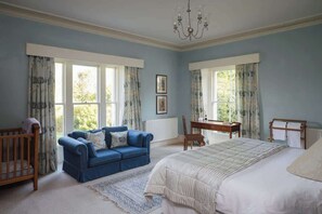 Une chambre à coucher avec un grand lit, un canapé bleu, une chaise en bois et un berceau.