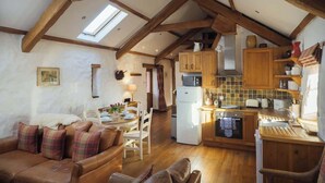 Un espace de vie chaleureux de style loft, comprenant un coin repas, une cuisine et des poutres apparentes.