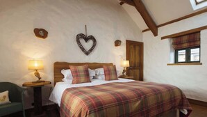 Une chambre avec un grand lit, deux tables de chevet avec des lampes, un élément décoratif en forme de cœur accroché au mur, et une fenêtre avec un rideau à carreaux.
