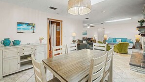 A dining area with a wooden table and chairs, a ceiling fan, and a view of the living room. - Aqua Queen - Pool 3BR (St. Augustine)