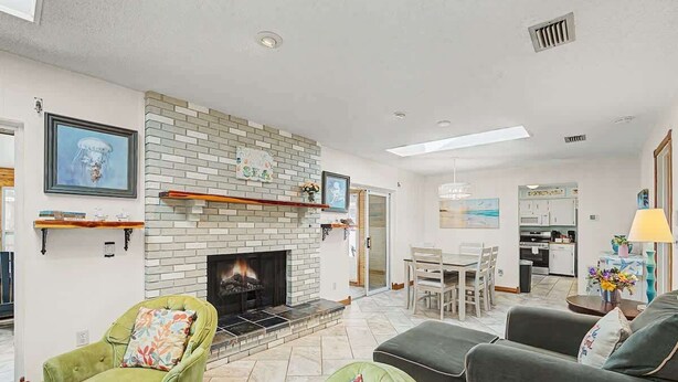 A living room with a fireplace, green armchairs, a grey sofa, and a dining area with a table and chairs. - Aqua Queen - Pool 3BR (St. Augustine)