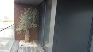 Un edificio moderno con balcone in vetro, un albero e una porta di colore scuro.