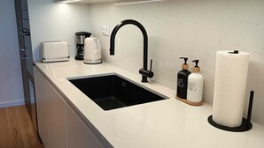 Una cucina moderna con un piano di lavoro bianco, lavello nero ed elettrodomestici in acciaio inossidabile.