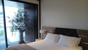 Camera d'albergo moderna con un letto grande, un comodino e una finestra vista su un albero e un edificio.