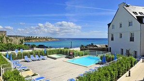 Un espace piscine aménagé sur le toit, avec des chaises longues et une vue sur la mer.