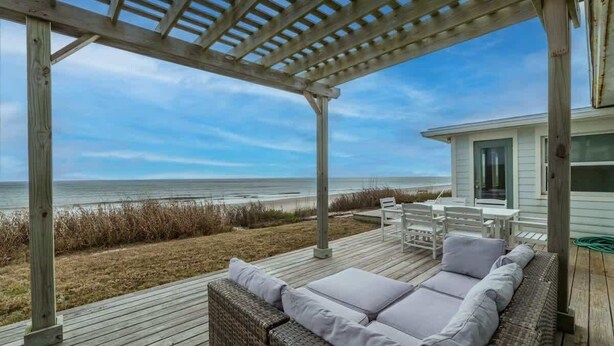 A covered outdoor seating area with a view of the beach, a wooden deck, and a building with large windows. - Blue Horizon House - 3BR Oceanfront (Ponte Vedra Beach)