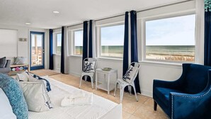 A room with a bed, two chairs, a small table, and a view of the beach. - Blue Horizon House - 3BR Oceanfront (Ponte Vedra Beach)