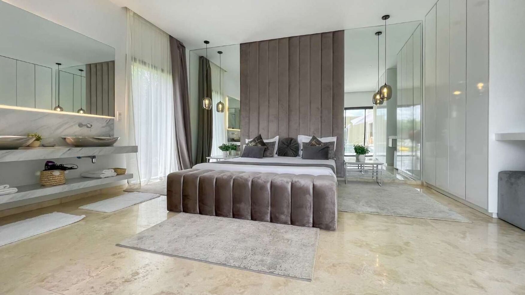 A modern bedroom with a large bed, a vanity with a mirror, and a view of the city through large windows.