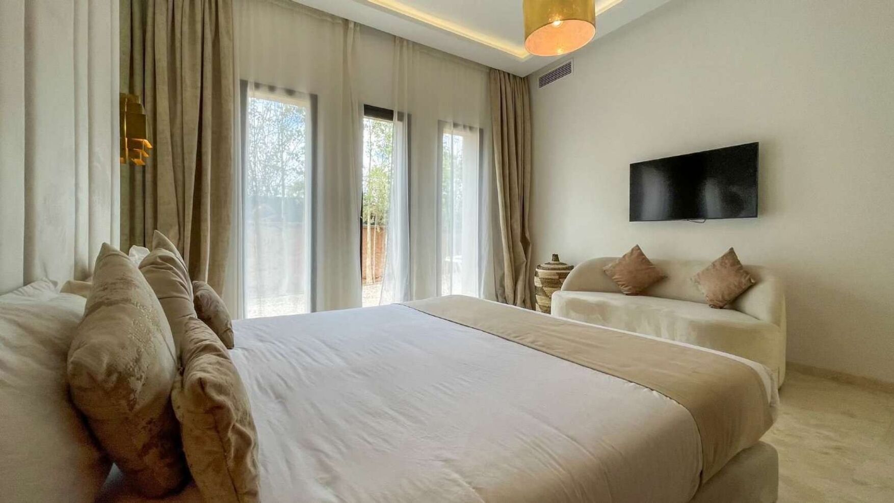 Une chambre à coucher avec un grand lit, un canapé, un téléviseur fixé au mur et une fenêtre avec des rideaux.