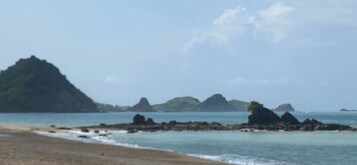 Uma praia com afloramentos rochosos e montanhas ao longe.