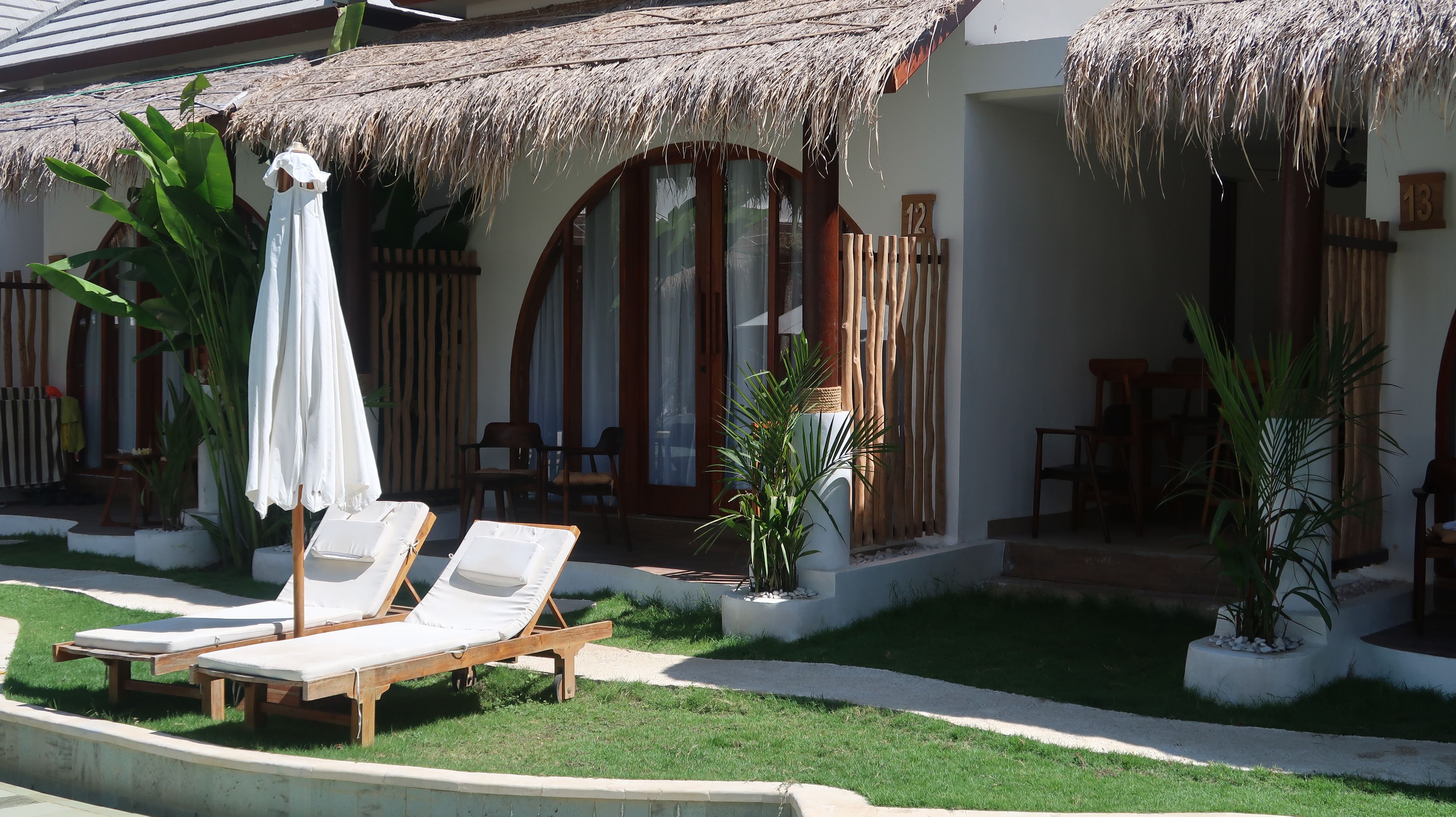 A resort with thatched-roof structures, lounge chairs, and potted plants.