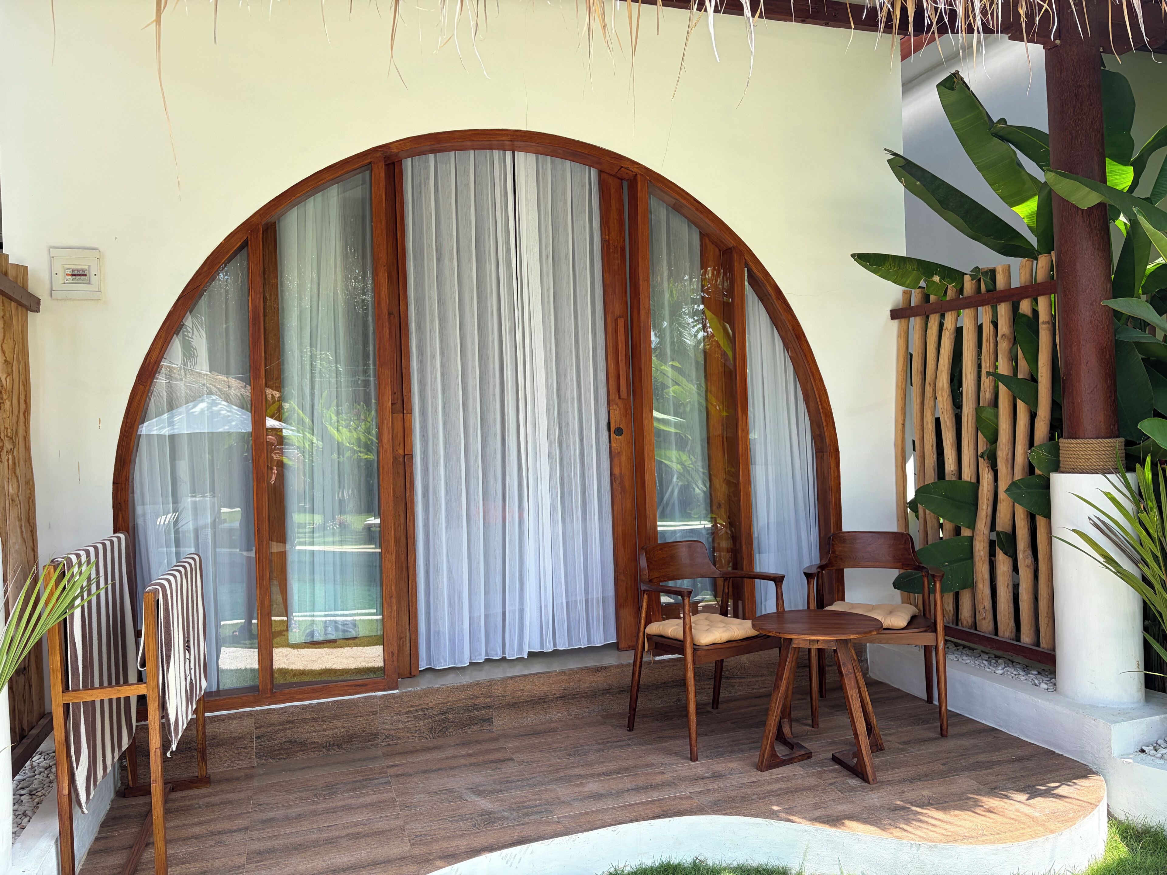 A wooden-framed glass door with curtains, a round wooden table with chairs, and a potted plant.