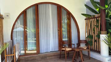 A wooden-framed glass door with curtains, a round wooden table with chairs, and a potted plant.