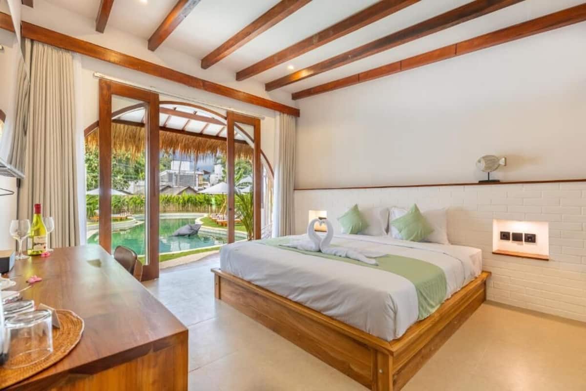 A bedroom with a bed, a wooden desk, and a view of an outdoor pool area.