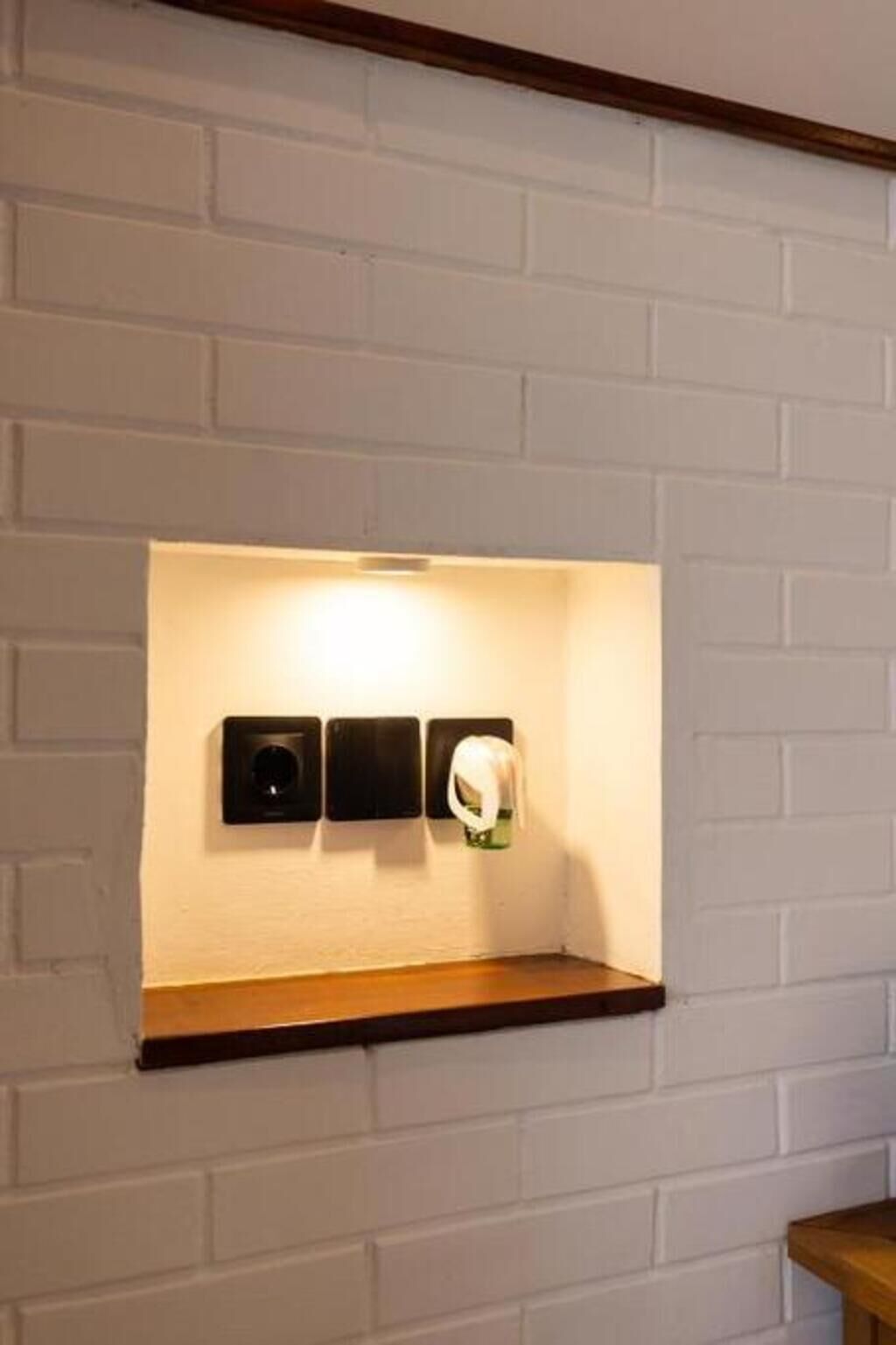 A white brick wall with a shelf containing a speaker, a small white object, and a green container.