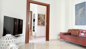 Ein Wohnzimmer mit Fernseher, einer Couch, einem Poster und einer Tür zu einem anderen Raum.