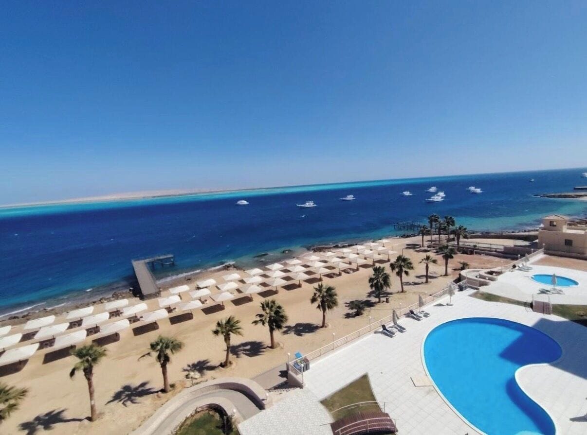 A resort with a pool, beach umbrellas, and a view of the ocean.
