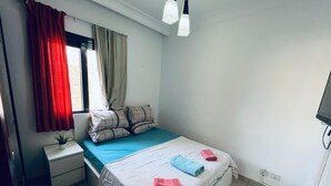 Una camera da letto con un letto, un comodino, una finestra con tende e una lampada a soffitto.