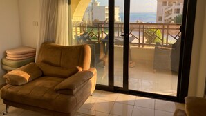 Un soggiorno con un divano e una porta vetrata scorrevole che dà su un balcone con vista su edifici e un corpo d'acqua.