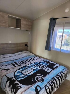 A bedroom with a bed, a built-in shelf, a window with curtains, and a view of the outside. - Cosy tiny house - Dune du Pilat - La Teste (La Teste-de-Buch)