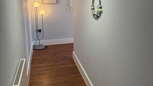 A hallway with wooden flooring, a radiator, a pendant light, a wall-mounted light fixture, and a framed picture. - Christchurch Apartment, Great Location With Parking (Christchurch)