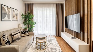A modern living room with a sofa, a round coffee table, a TV on a wooden wall, and a large plant. - RentPlanet - Apartament Przemysłowa (Katowice)