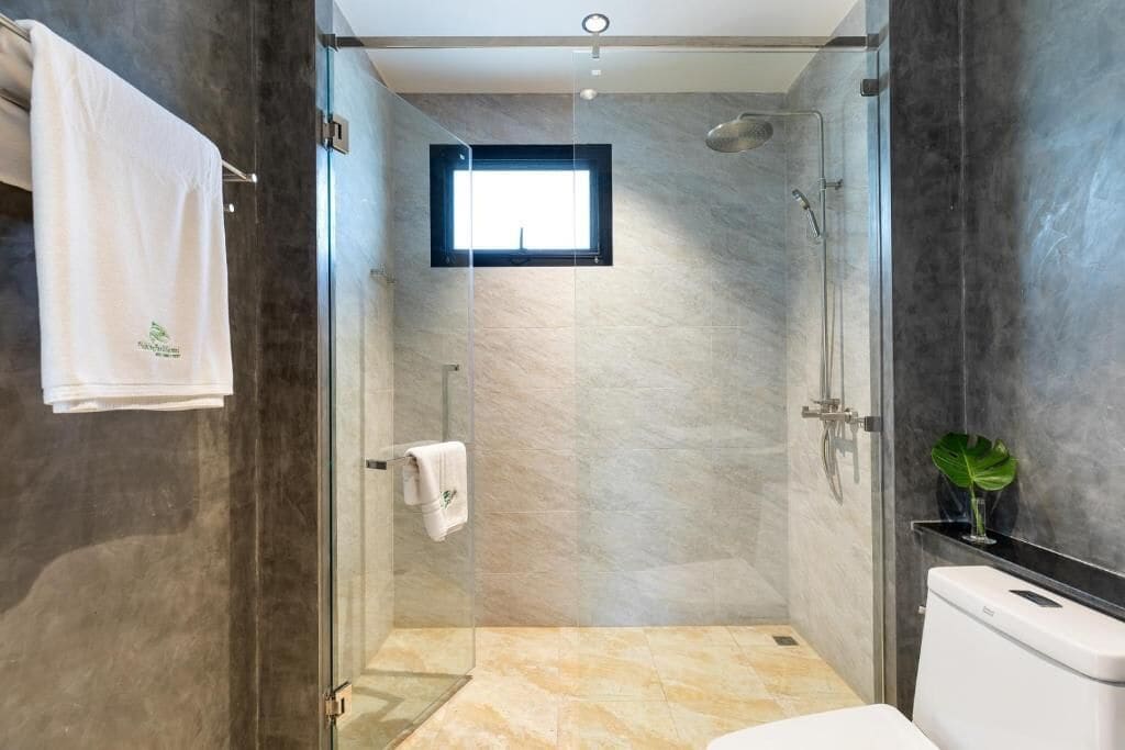 A modern bathroom with a glass-enclosed shower, a visible window, and a toilet.