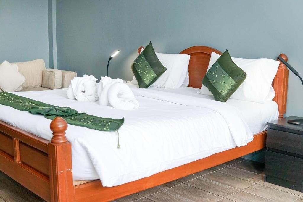 A neatly made bed with white linens, a wooden headboard, and green decorative pillows.