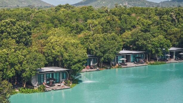 Ein Resort mit mehreren Gebäuden, umgeben von üppiger Vegetation und einem türkisfarbenen Pool.