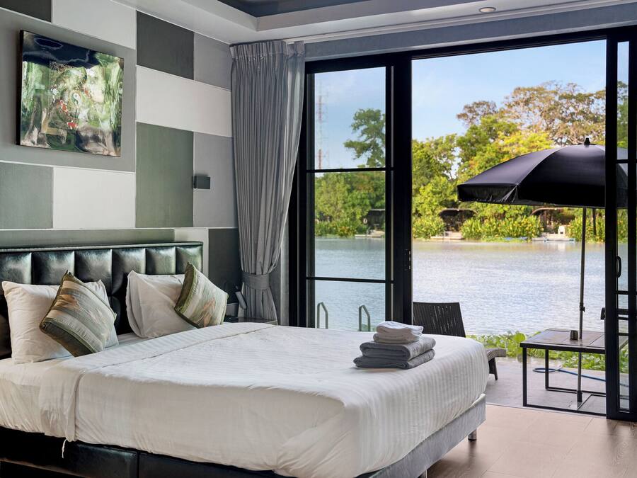 A modern bedroom with a large bed, a view of a lake, and a dining area with an umbrella.