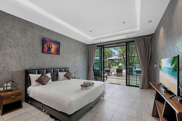 A modern bedroom with a large bed, a TV, and a sliding glass door leading to an outdoor area. - Samui Fishing Club & Resort (Koh Samui)