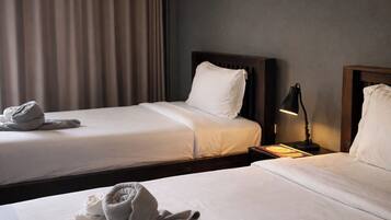 A hotel room with two beds, a nightstand with a lamp, and a window with curtains.