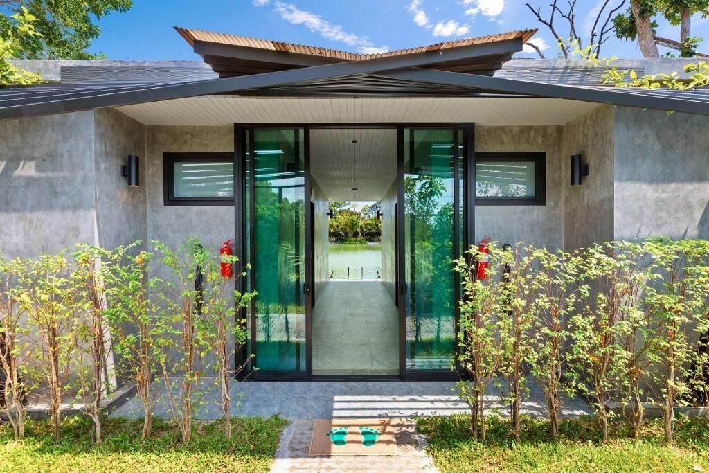 Un bâtiment moderne doté d’une entrée en verre, d’une façade en béton et d’un chemin menant à l’entrée.