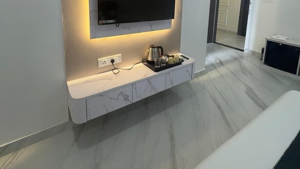 Un salon moderne avec un téléviseur à écran plat fixé à un mur en marbre, une console blanche sur laquelle se trouve une bouilloire, et un sol en marbre.