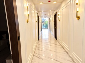 Ein Hotelgang mit Marmorböden, Wandleuchten und Türen zu Zimmern.
