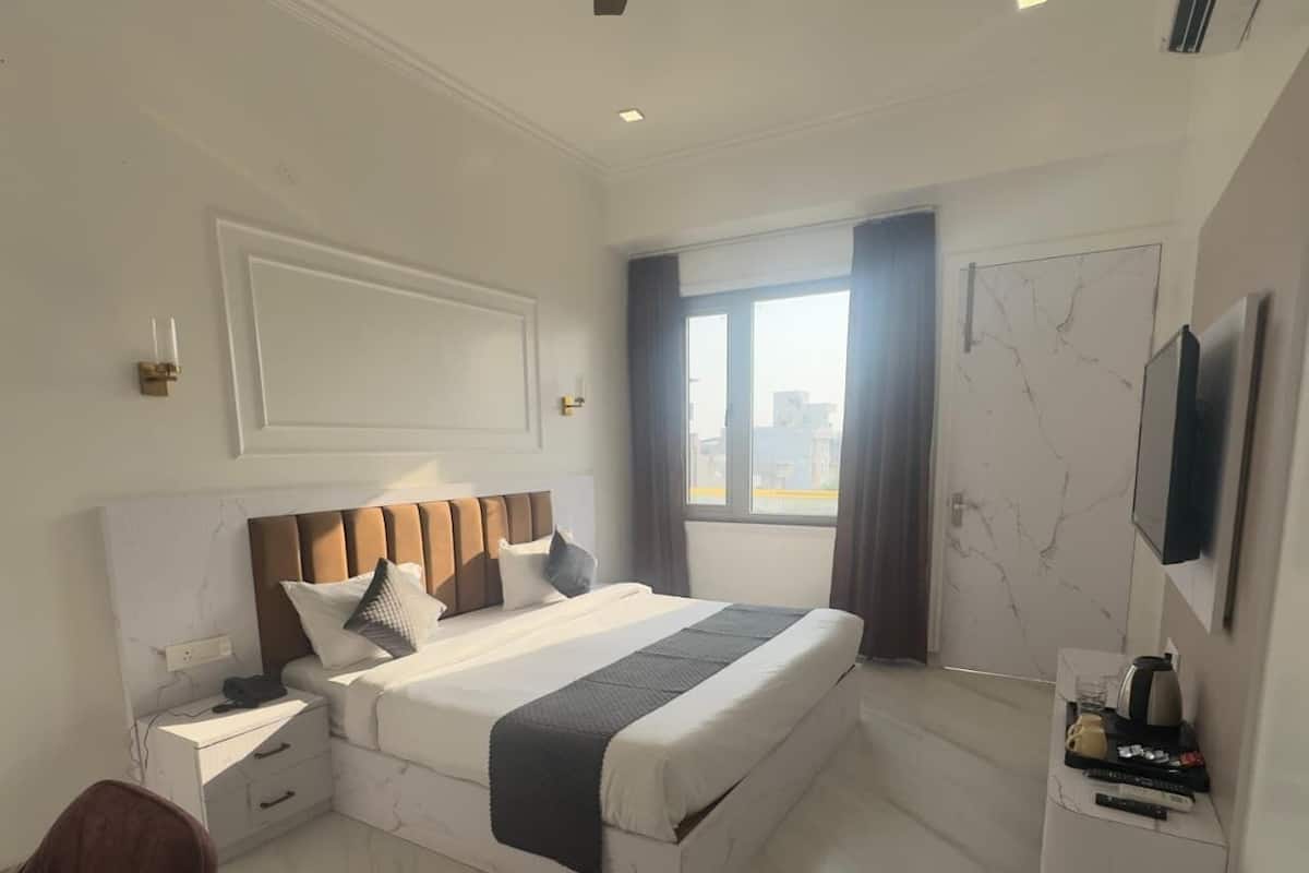 Ein modernes Hotelzimmer mit einem großen Bett, einem Flachbildfernseher, einem Schreibtisch mit Stuhl und einem Fenster mit Vorhängen.