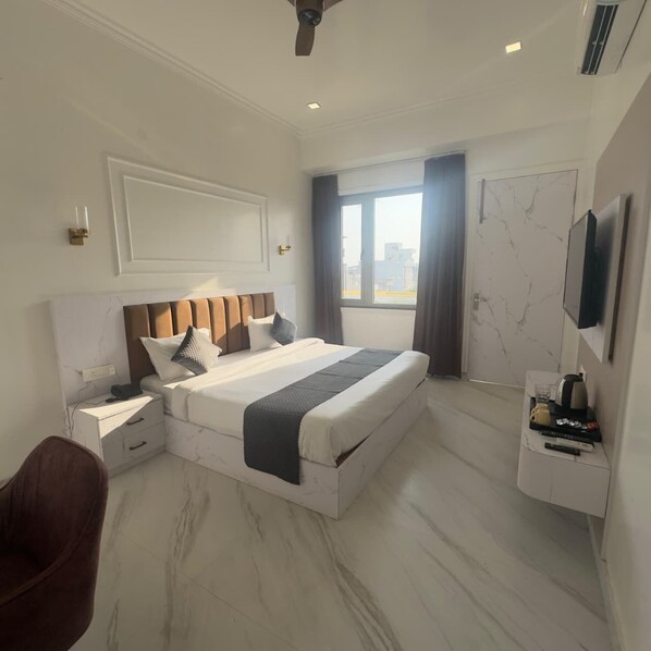 A modern hotel room with a large bed, a flat-screen TV, a desk with a chair, and a window with curtains.