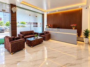 Een hotel receptie met een receptiebalie, zithoek en een groot raam.